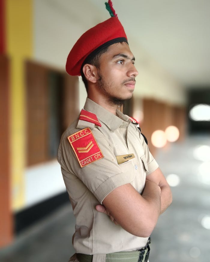 A young cadet in uniform posing with arms crossed indoors, embodying discipline.